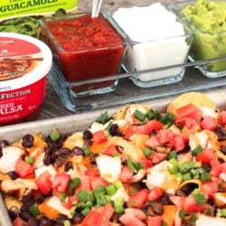 Easy Oven Nachos on a cookie sheet with sour cream, salsa, and guacamole in the background.