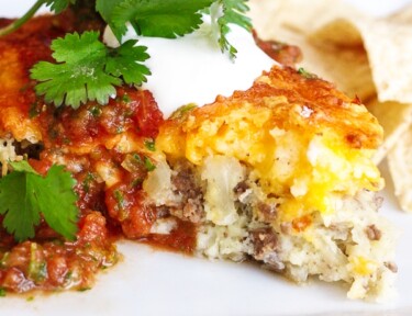 Easy Taco Pie topped with sour cream, salsa, and cilantro with chips in the background.