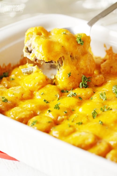 Tater tot casserole in baking dish with ground beef, green beans, tater tots, and cheese.