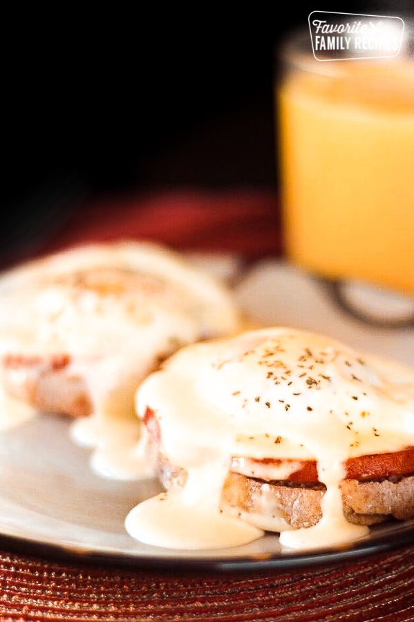 Foolproof Eggs Benedict on a plate with orange juice in the background.