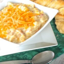 Loaded Baked Potato Soup in a white bowl with a spoon and breadsticks on the side.