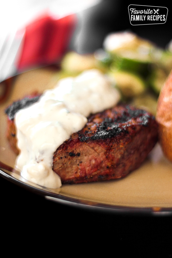Filet Mignon topped with Melted Blue Cheese Sauce on a tan plate.