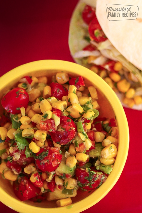 Fresh Corn Salsa in a yellow bowl with tortillas in the background.