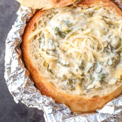 spinach artichoke dip in a bread bowl with foil covering