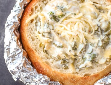 spinach artichoke dip in a bread bowl with foil covering