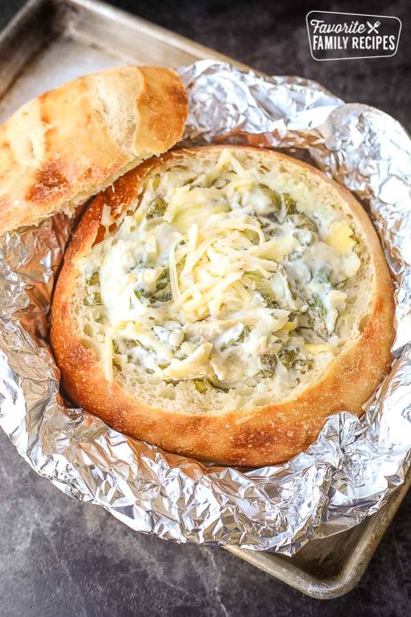 spinach artichoke dip in bread bowl with top to the side, foil covering