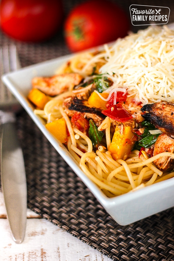 Grilled Chicken Pasta Primavera topped with cheese in a white bowl.