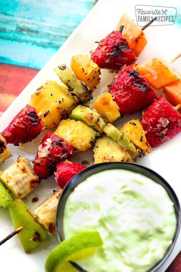 3 Grilled Fruit Kabobs with Key Lime Yogurt Dip on othe side all on a white plate.