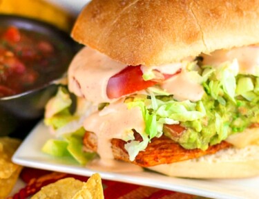 Guacamole Chicken Torta Sandwich on a white plate with chips and salsa on the side.