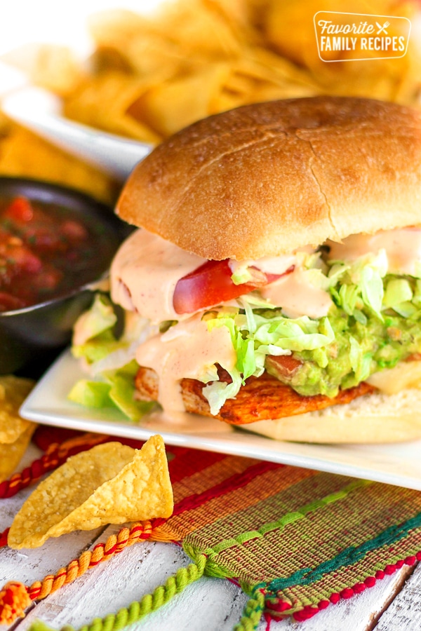 Guacamole Chicken Torta Sandwich on a white plate with chips and salsa on the side.