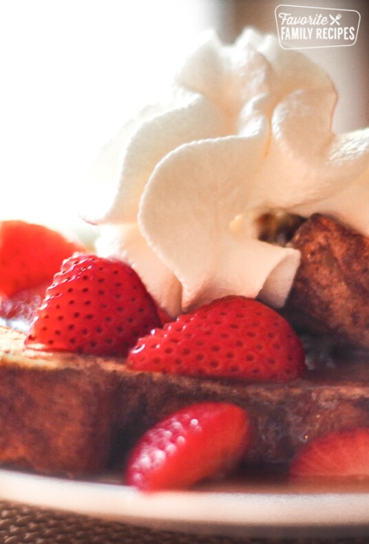 Close up of Kneaders French Toast topped with strawberries, whipped cream, and Caramel Syrup