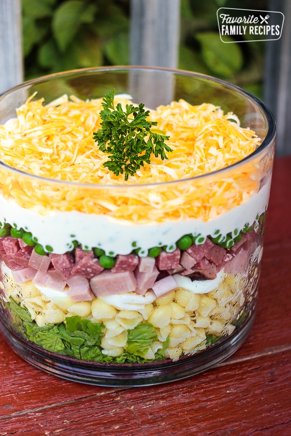 Layered Pasta Salad with ham, peas, noodles in a glass dish topped with cheese and a garnsih.