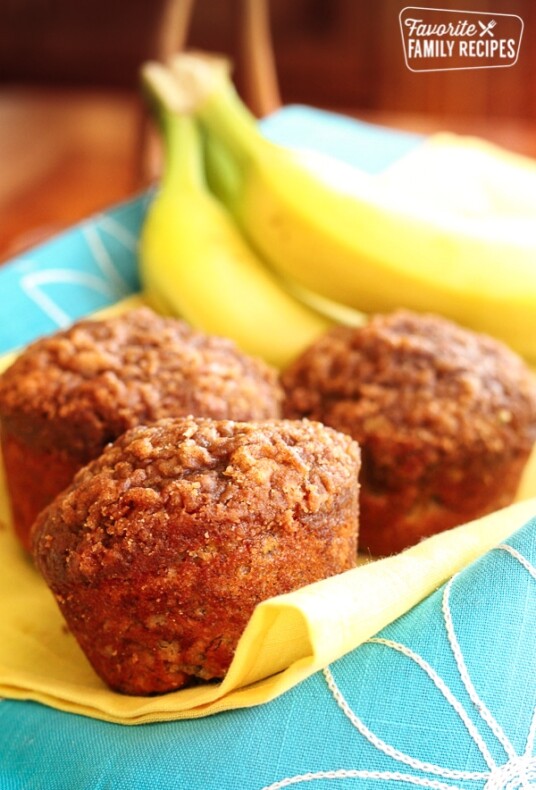 Lowfat Banana Crumb Muffins on a yellow and blue cloth with bananas in the background.