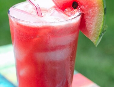 A glass of Melonade with a straw and watermelon slice.