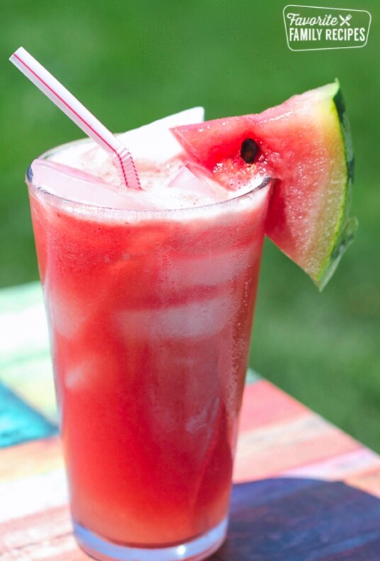 A glass of Melonade with a straw and watermelon slice.