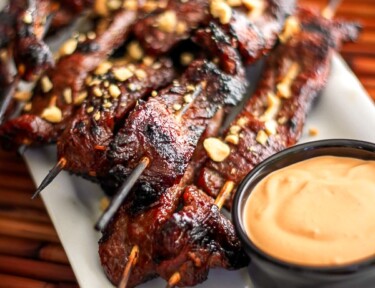 Mongolian Beef Satay with a side of dipping sauce on a white tray.