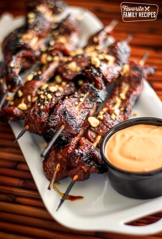 Mongolian Beef Satay with a side of dipping sauce on a white tray.