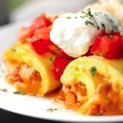 Omelette Roll Ups topped with sour cream and tomatoes on a white plate.