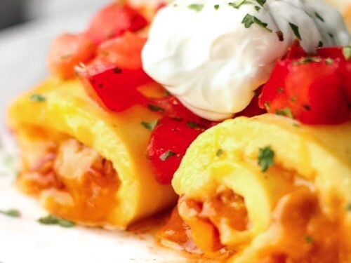 Omelette Roll Ups topped with sour cream and tomatoes on a white plate.