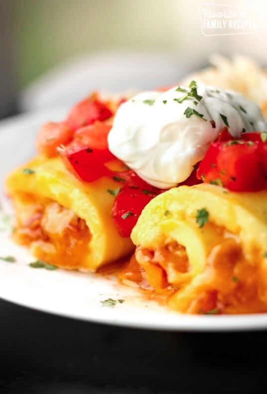Omelette Roll Ups topped with sour cream and tomatoes on a white plate.