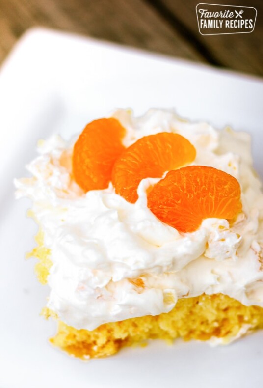 A slice of Orange Pineapple Cake topped with mandarin oranges on a white plate.