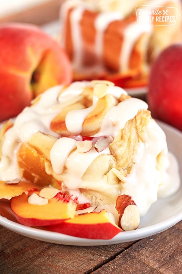 Peaches and Cream Cinnamon Roll with a couple peach slices on the side on a white plate.