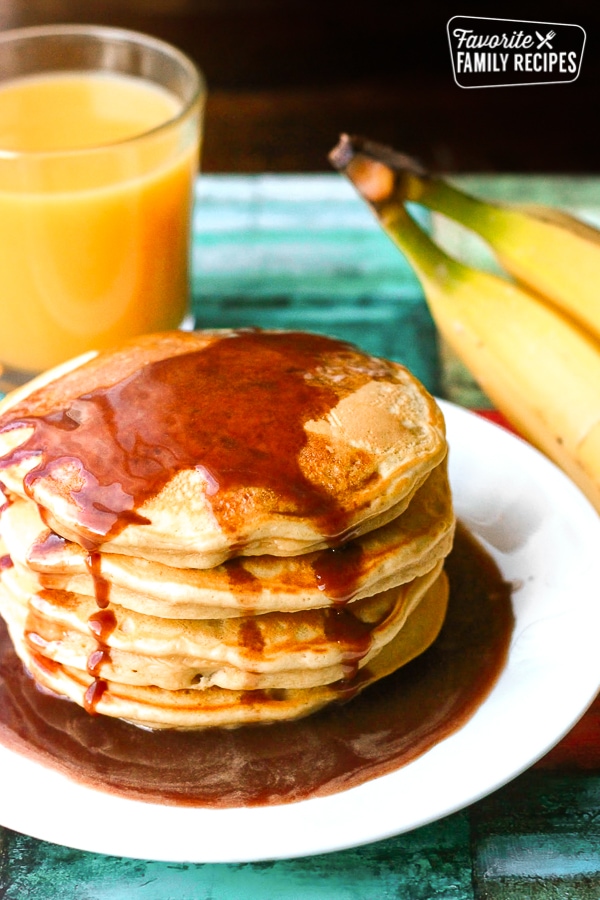 Peanut Butter Banana Pancakes with Nutella Syrup on a white plate with a glass of orange juice in the background.