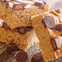Peanut Butter Cup Rice Krispie Treats stacked on top of each other with peanut butter cups on the side.
