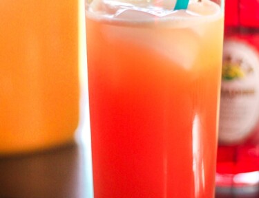 A Pomegranate sunrise drink in a clear glass cup with a blue straw