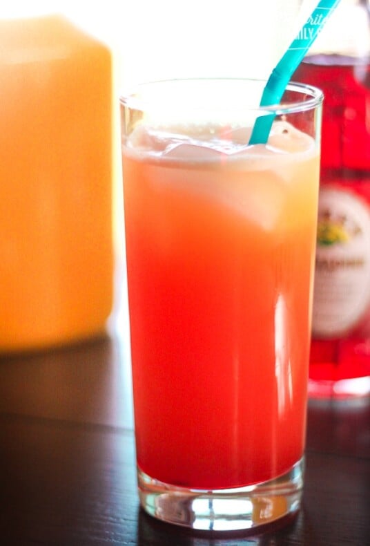 A Pomegranate sunrise drink in a clear glass cup with a blue straw