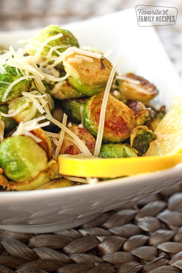 Sauteed lemon garlic brussels sprouts in a white bowl with a lemon slice. 