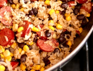 A skillet filled with sausage and rice with black beans and corn