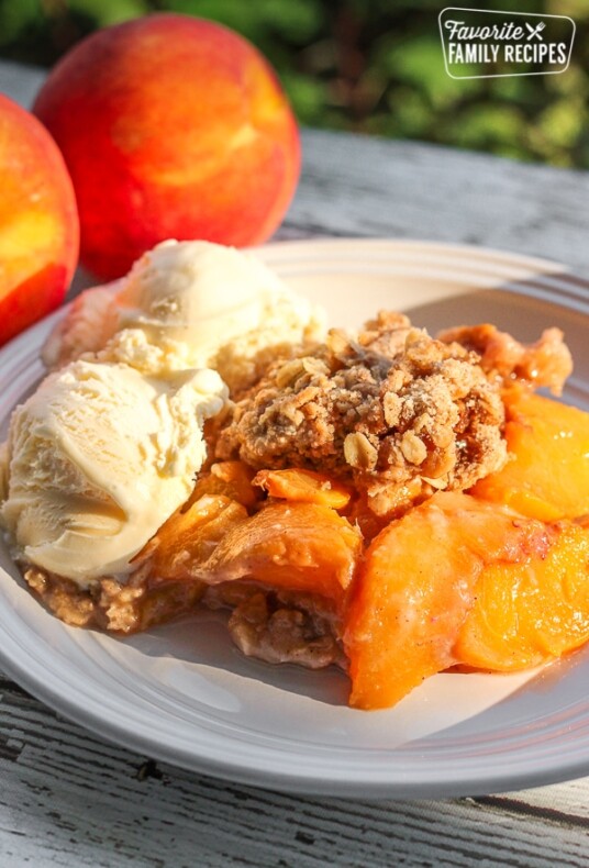 Crock Pot Peach Cobbler served with two scoops of vanilla ice cream with fresh peaches in the background