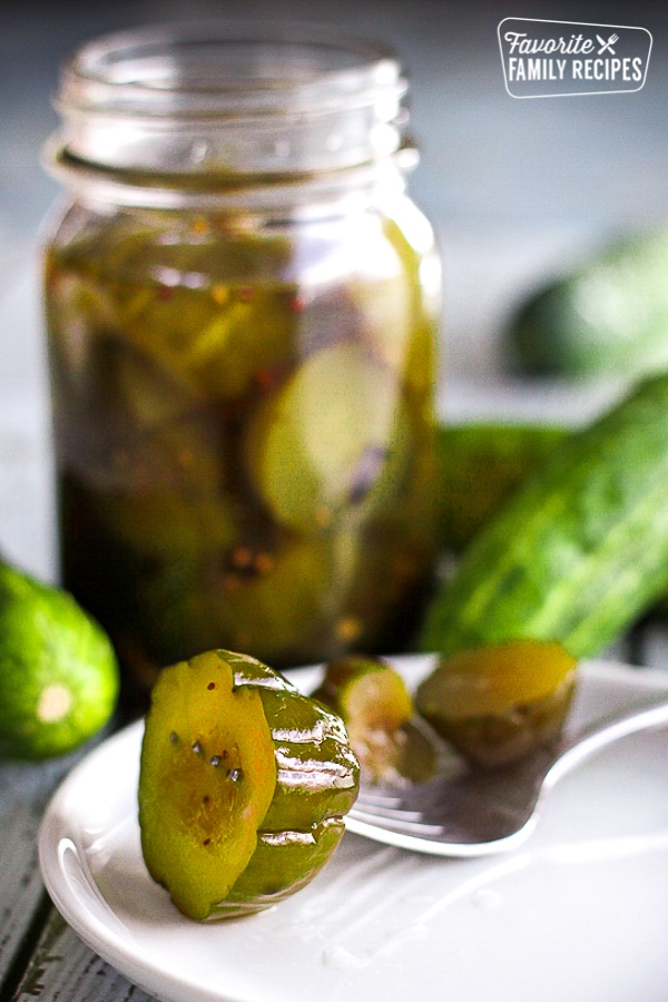 A jar of sweet pickles with a slice of pickle on a fork. 
