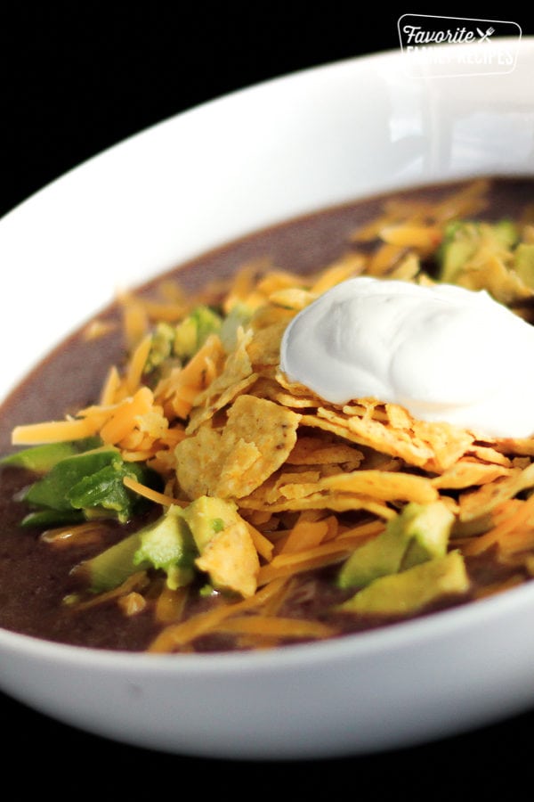 Black Bean Soup with corn chips, avocado and a dollop of sour cream in white bowl.