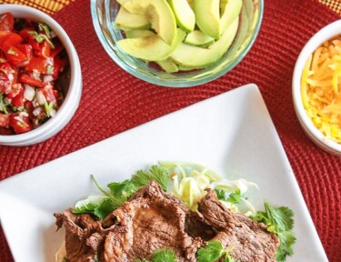 Grilled Carne Asada on a plate with avocado, cheese, and salsa on the side.