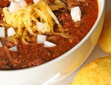 Cheater Chili topped with cheese and onions in a white bowl with cornbread on the side.