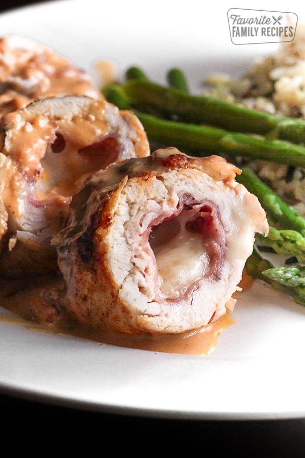 Chicken Cordon Bleu sliced open with asparagus and brown rice on the side all on a white plate.