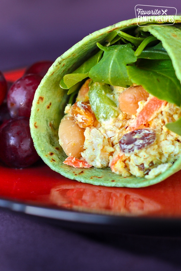 Chicken Salad Curry Wrap with grapes on the side on a red plate.