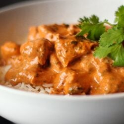 Chicken Tikka Masala over white rice in a white bowl with a garnish.