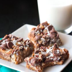 3 Coconut Pecan Cookie Bars on a white plate with a glass of milk in the background.