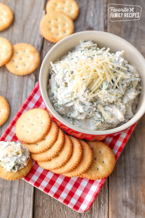 top shot of crackers on a plate with easy spinach dip in a red bowl