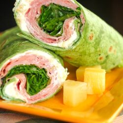 2 Ham Pineapple Wraps stacked on top of each other with a side of pineapple on a yellow plate.