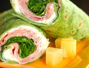 2 Ham Pineapple Wraps stacked on top of each other with a side of pineapple on a yellow plate.