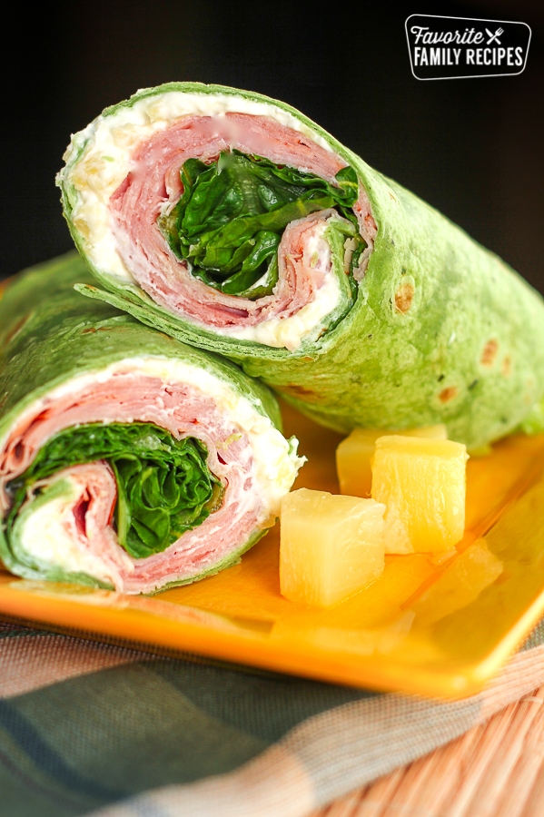 2 Ham Pineapple Wraps stacked on top of each other with a side of pineapple on a yellow plate.