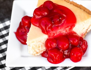 A slice of homemade cheesecake on a white plate topped with cherries