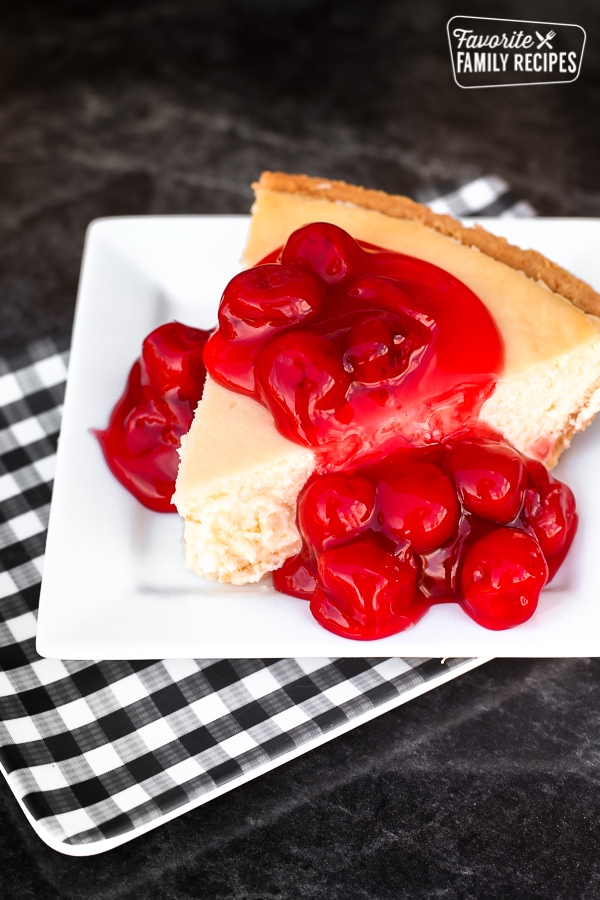 A slice of homemade cheesecake on a white plate topped with cherries