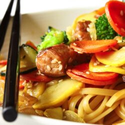 Oriental Pasta in a white bowl with chopsticks on the side.