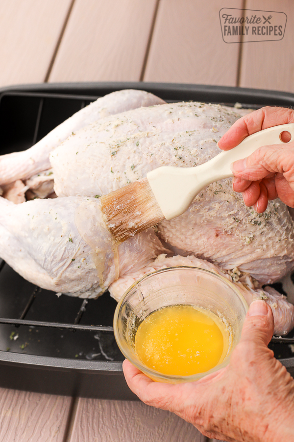 A raw, whole turkey being basted with melted butter and herbs