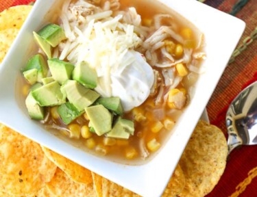 Chicken tortilla soup in bowl with sour cream and avocado with tortilla chips on the side.